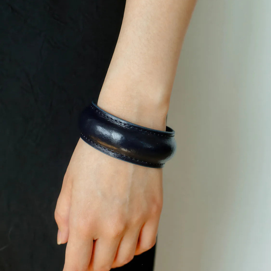 Black leather bracelet on a wrist against a neutral background
