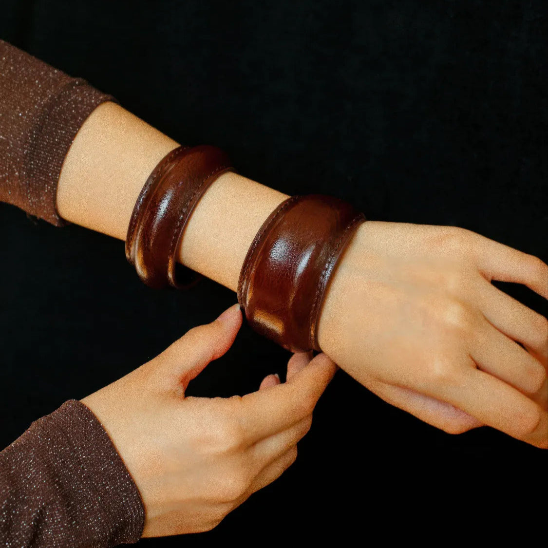 Person wearing brown leather arm bands on a black background