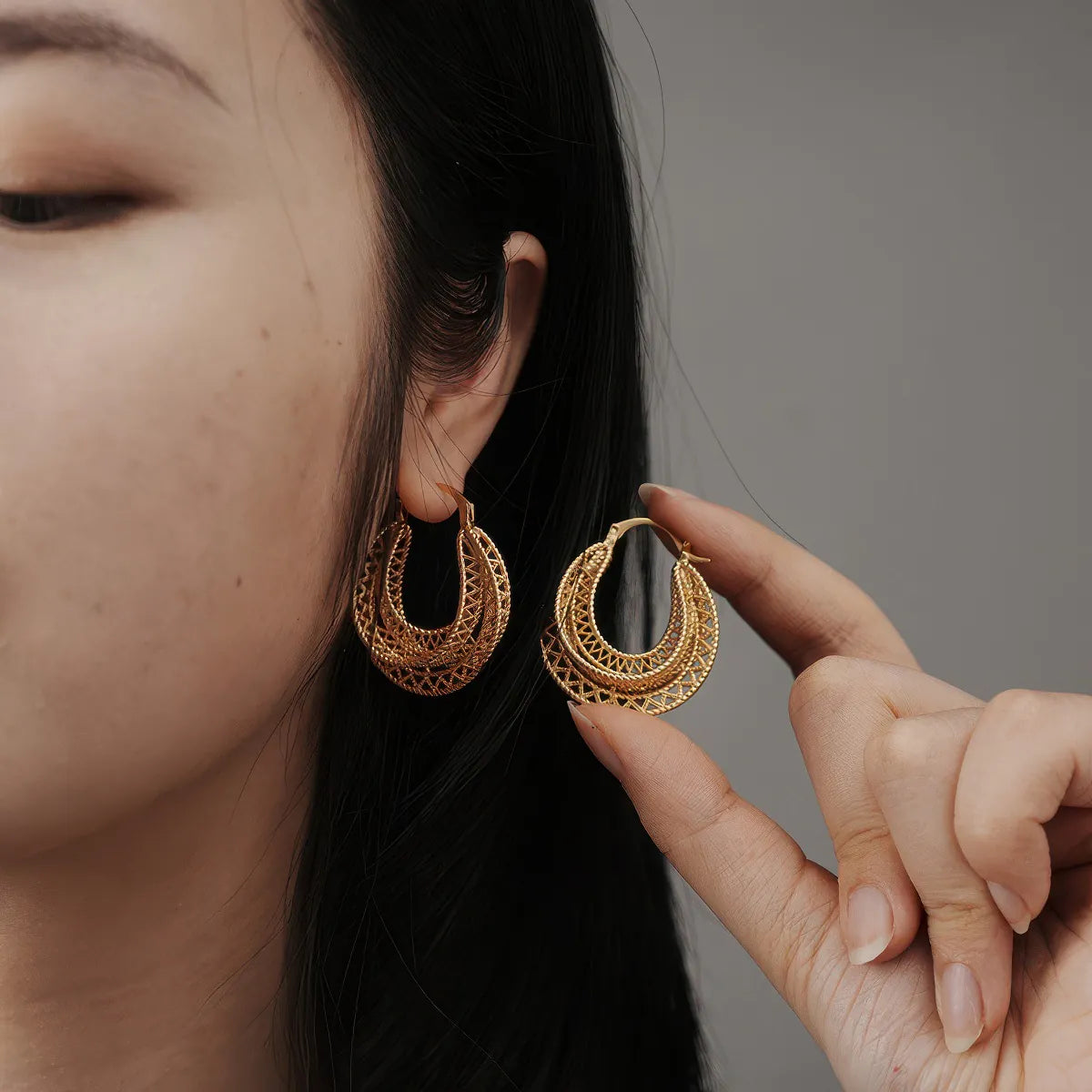 Close-up of a person wearing gold hoop earrings with a neutral background. #Style_A