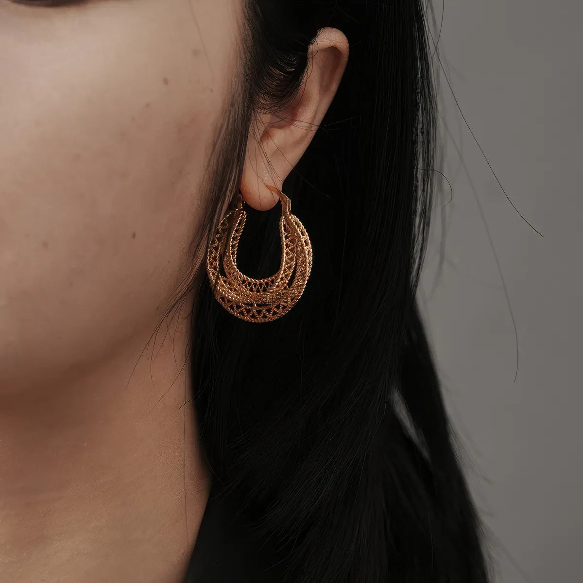 Close-up of a person wearing gold hoop earrings with a neutral background. #Style_A