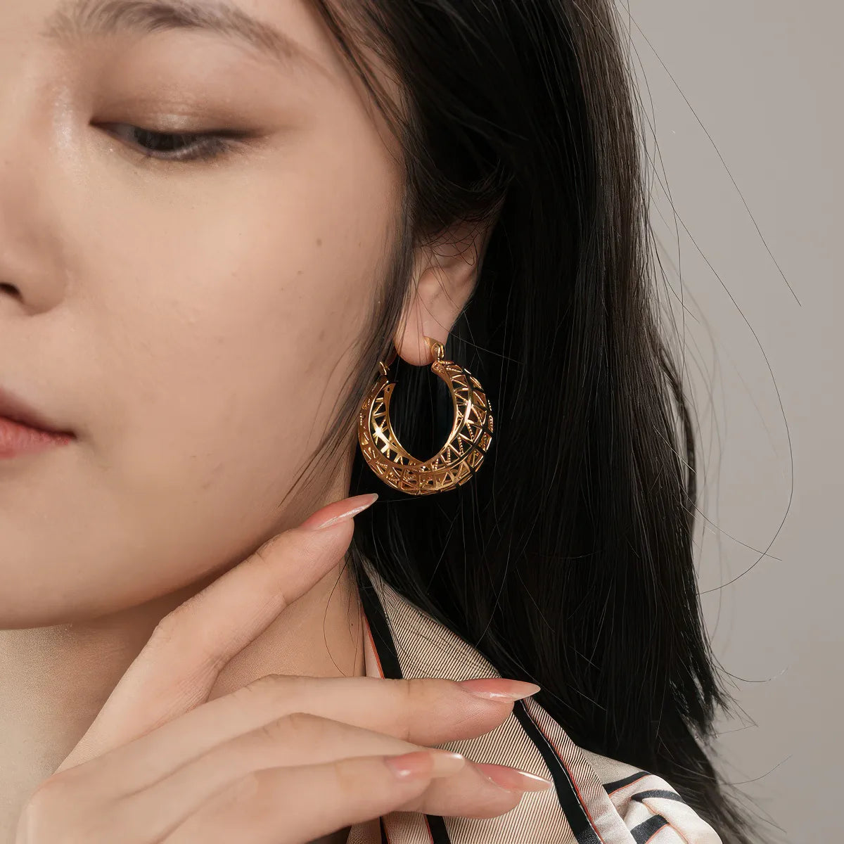 Close-up of a woman wearing gold hoop earrings with a neutral background. #Style_B