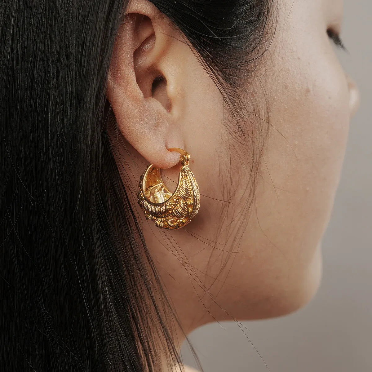 Close-up of a person wearing a gold hoop earring with intricate designs. #Style_C