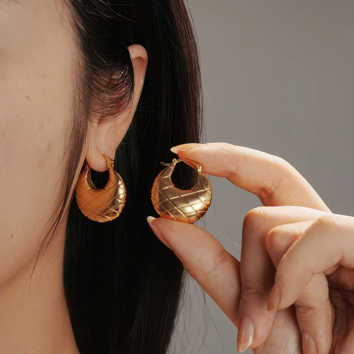 Gold hoop earrings being worn and held by a person with a neutral background. #Style_A