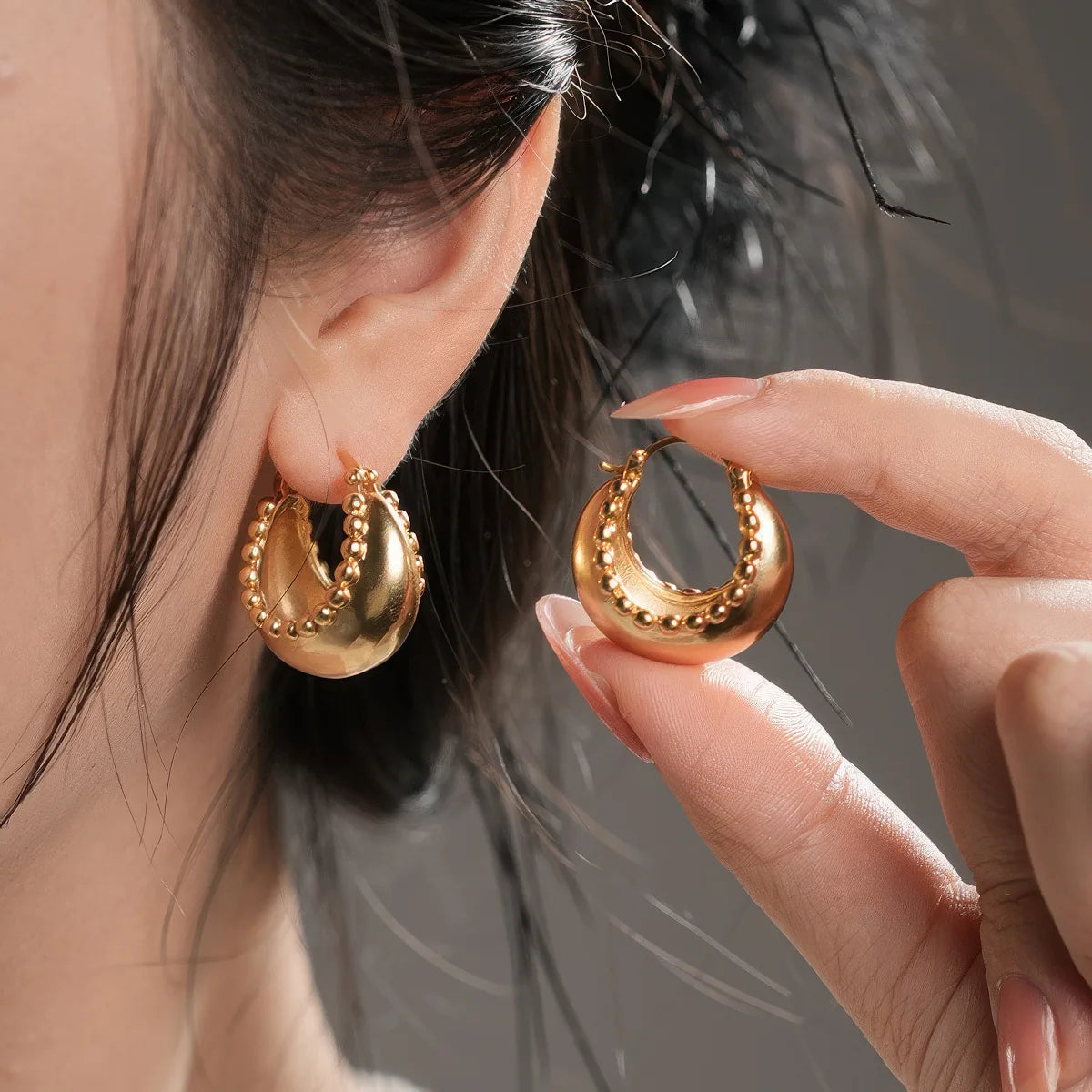 Gold hoop earrings worn by a person with a blurred background. #Style_C