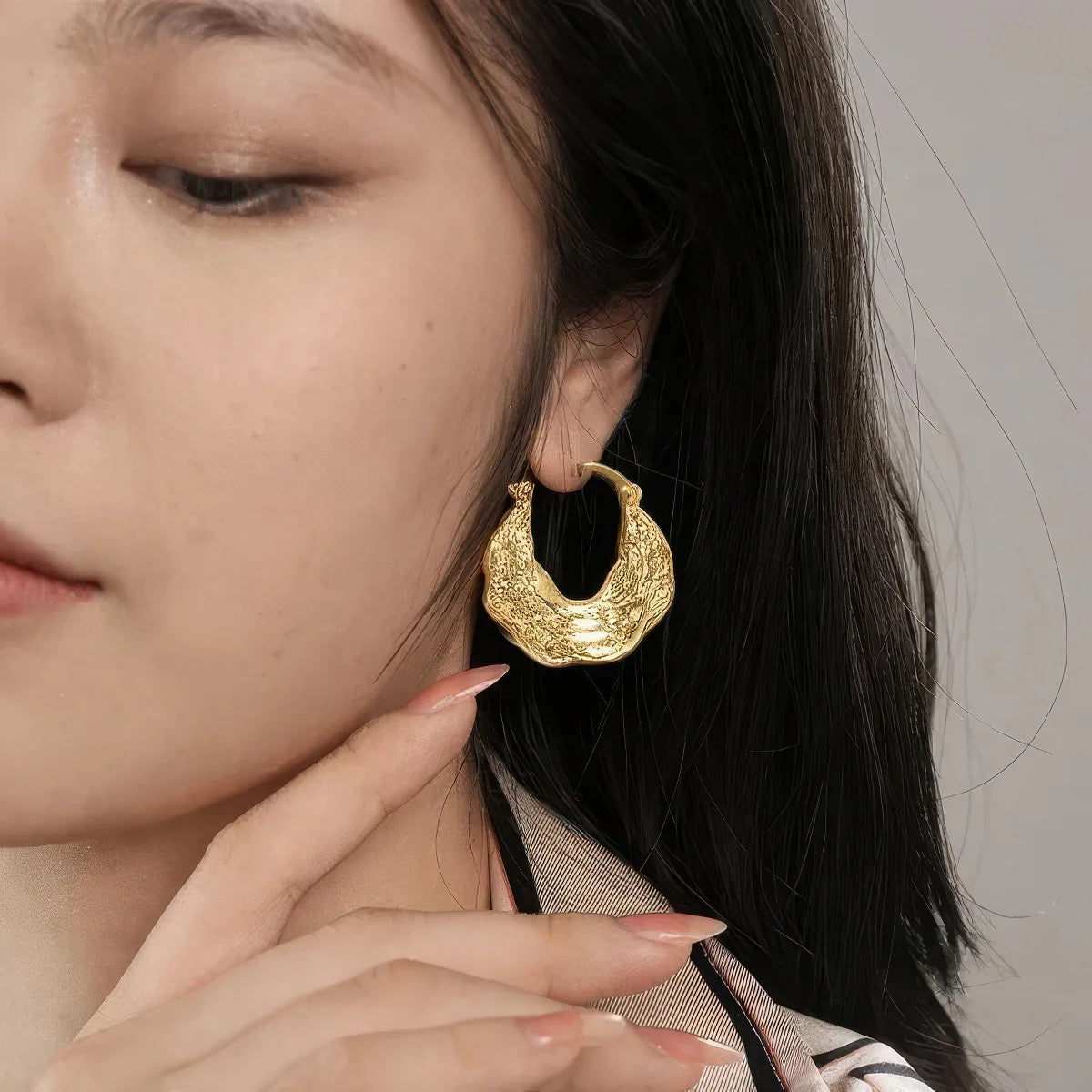 Close-up of a person wearing gold hoop earrings with a neutral background. #Style_D