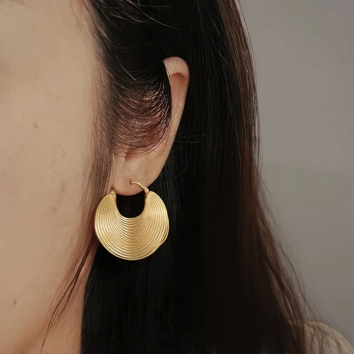 Gold hoop earring worn by a person with dark hair. #Style_E