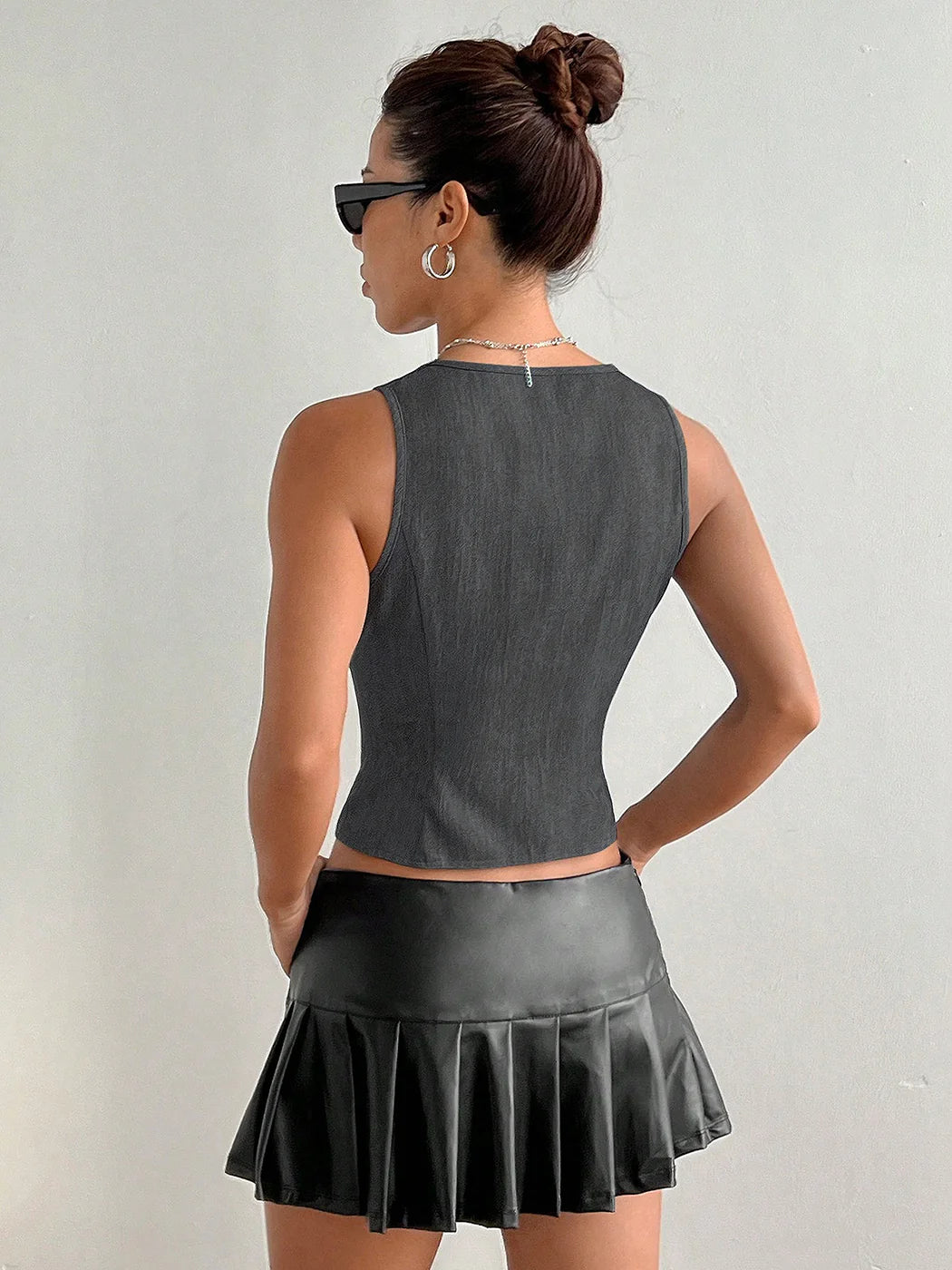 Woman wearing a gray sleeveless top and black pleated skirt against a plain background #Color_DarkGray