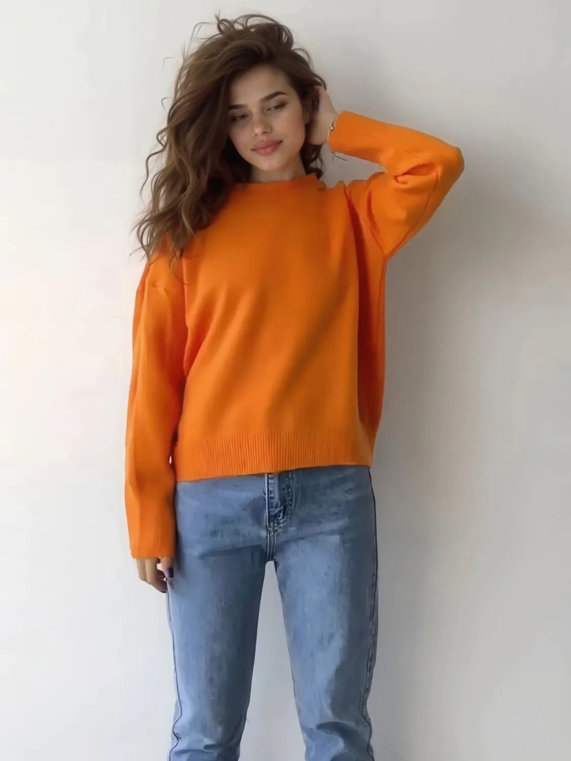 Woman wearing an orange sweater and blue jeans against a white background. #Color_Orange