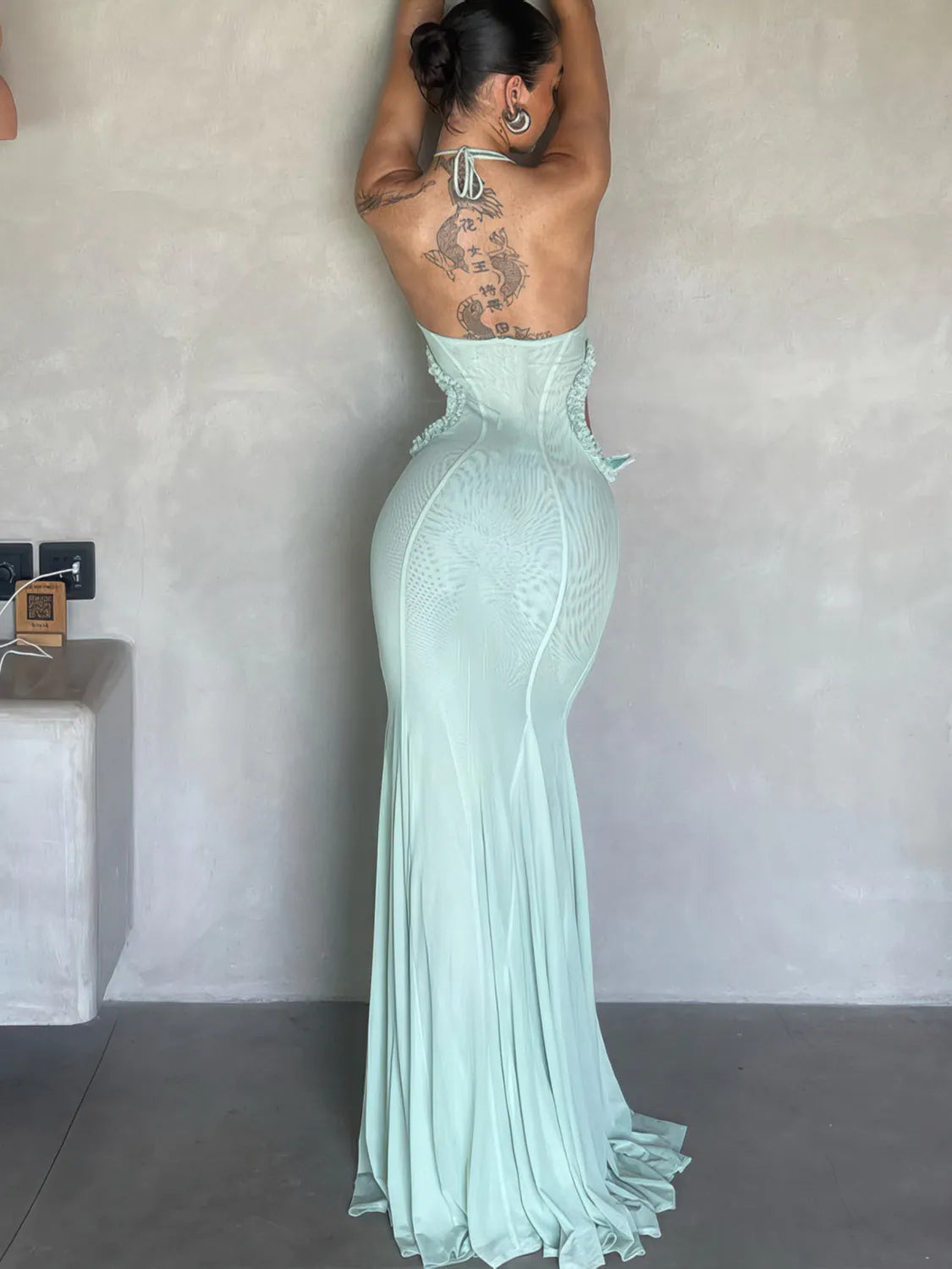 Mint green evening gown with a backless design, worn by a person against a plain wall. #Color_Green