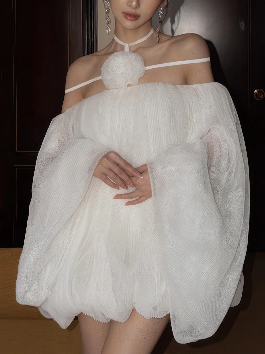 Woman wearing a white dress with sheer sleeves against a dark background. #Color_White