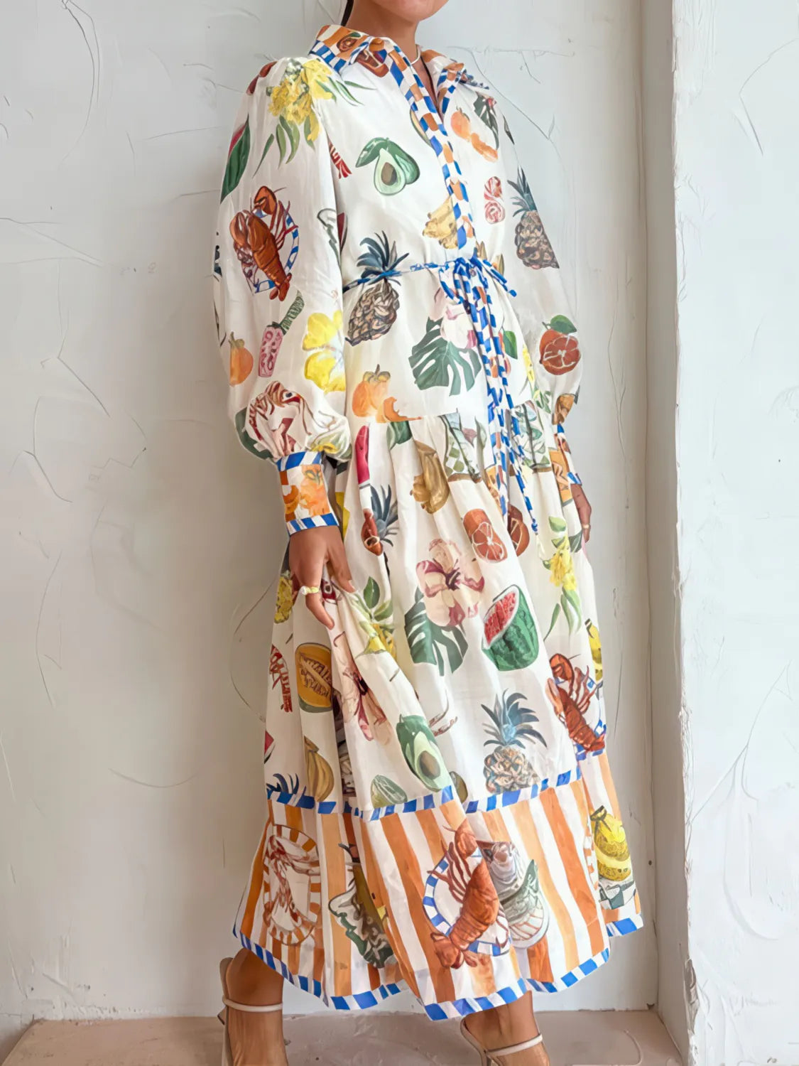 Colorful dress with fruit pattern worn by a person against a white wall. #Color_White