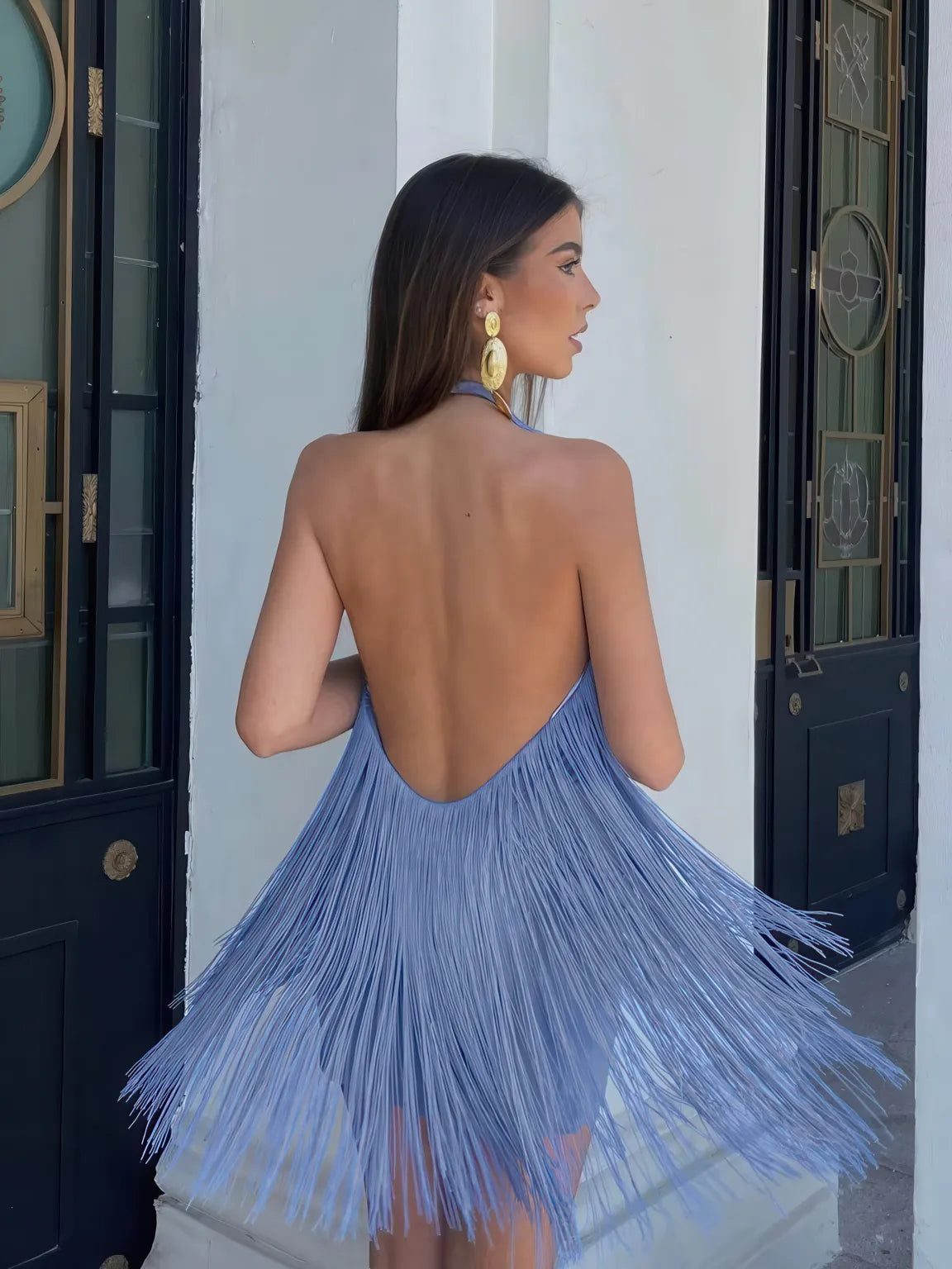 Woman wearing a blue fringe dress with a white door in the background. #Color_Blue