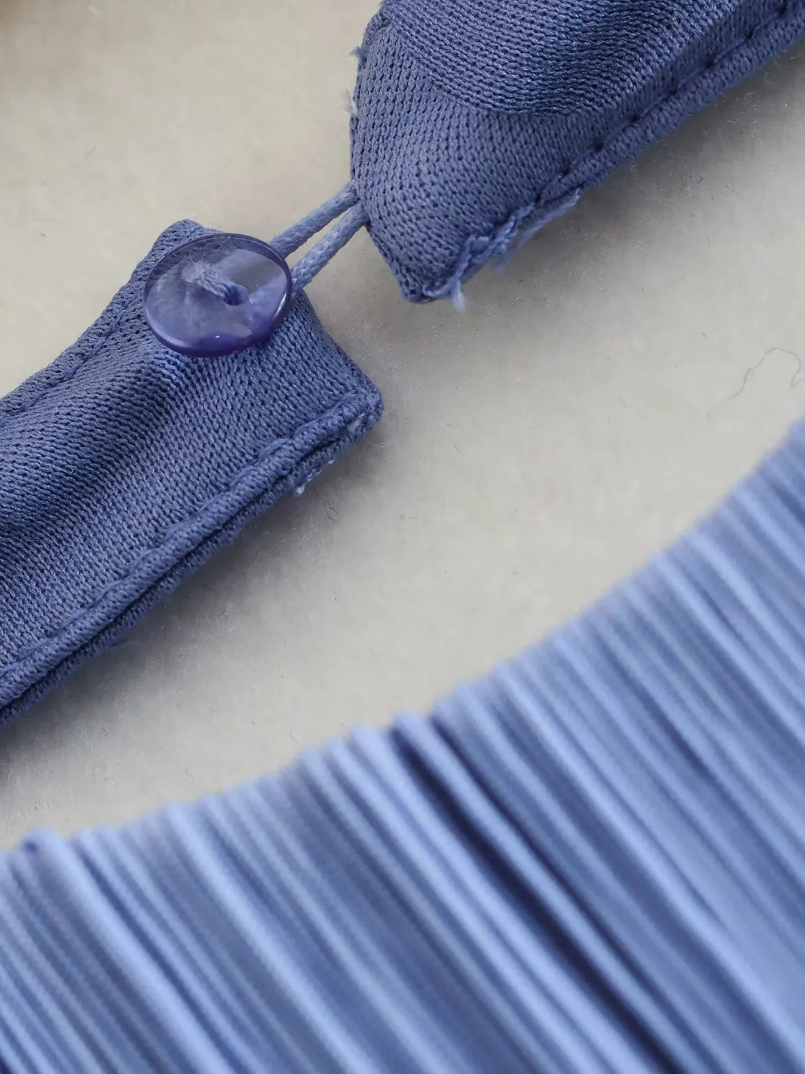 Close-up of a blue fabric garment with a button on a beige background. #Addtl