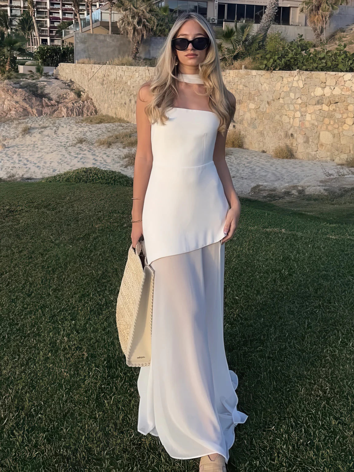 Woman in a white dress standing on grass with a scenic background. #Color_White