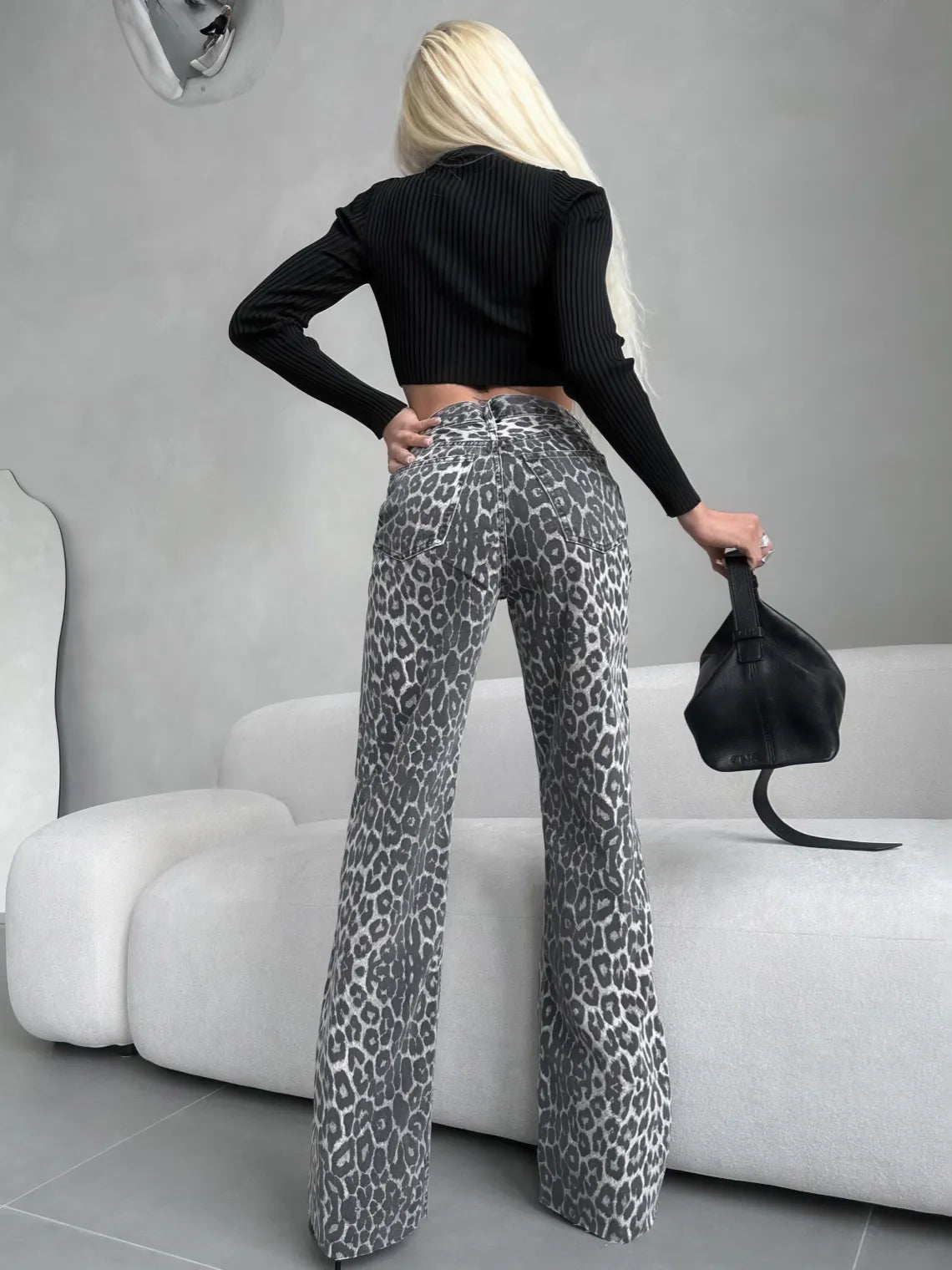Person wearing black crop top and leopard print pants holding a black handbag in a minimalistic setting. #Color_Gray