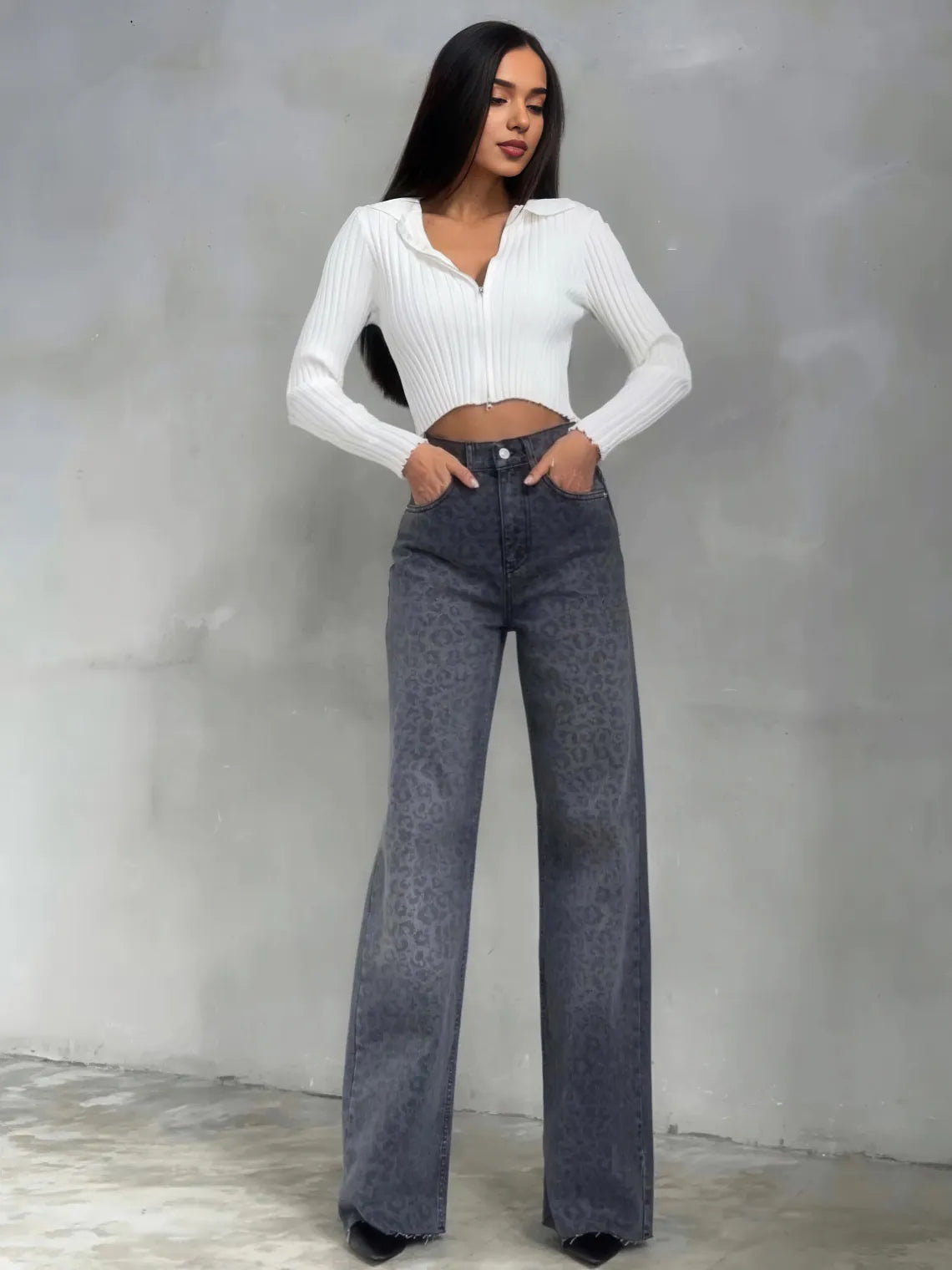 Woman wearing a white ribbed sweater and dark blue jeans against a gray background. #Color_DimGray