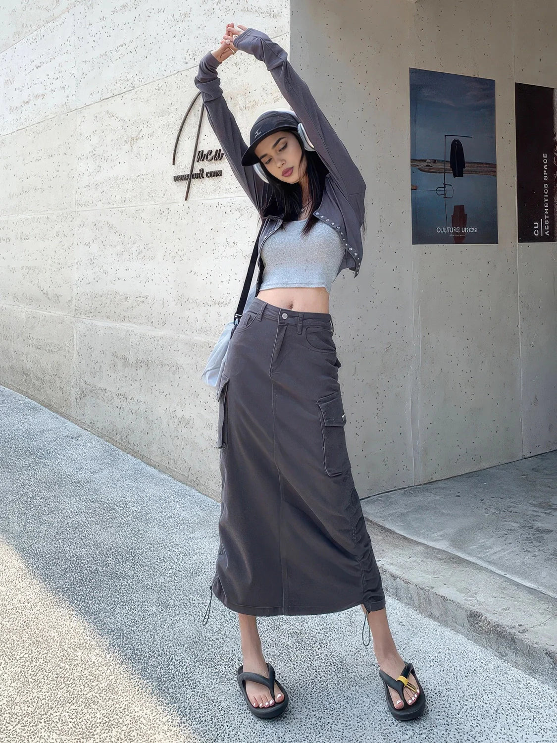 Person wearing a gray outfit with a long skirt and crop top, standing against a concrete wall. #Color_Gray