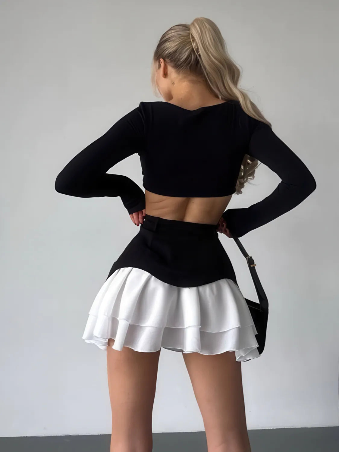 Person wearing a black long-sleeve top and white skirt against a plain background. #Color_Black