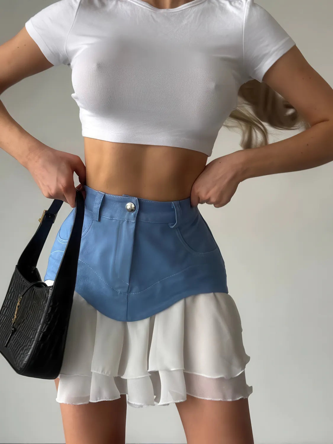 Person wearing a white crop top and blue and white layered skirt holding a black handbag. #Color_Blue