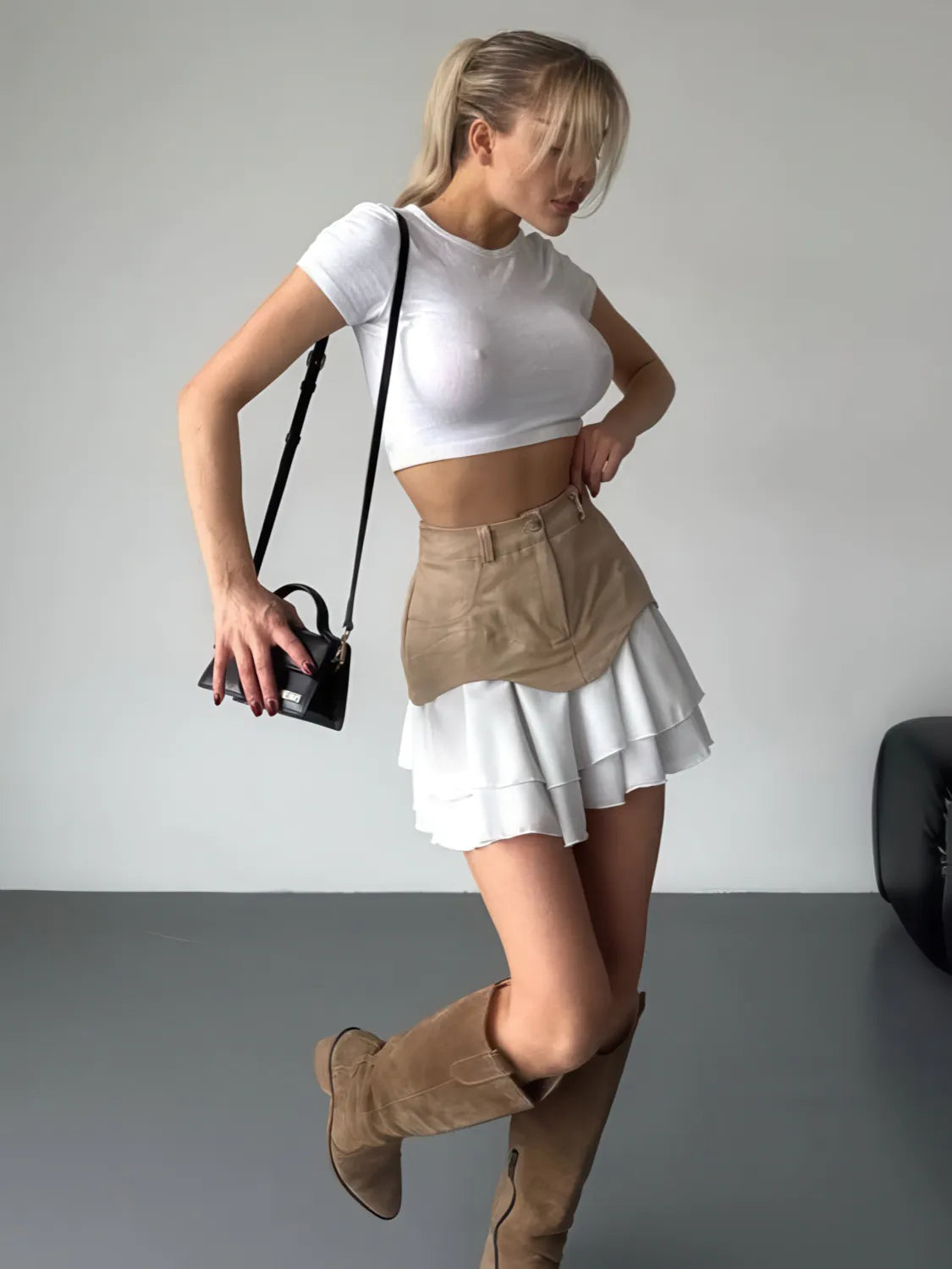 Woman wearing a white crop top, beige apron, white skirt, and brown knee-high boots against a plain background. #Color_Khaki