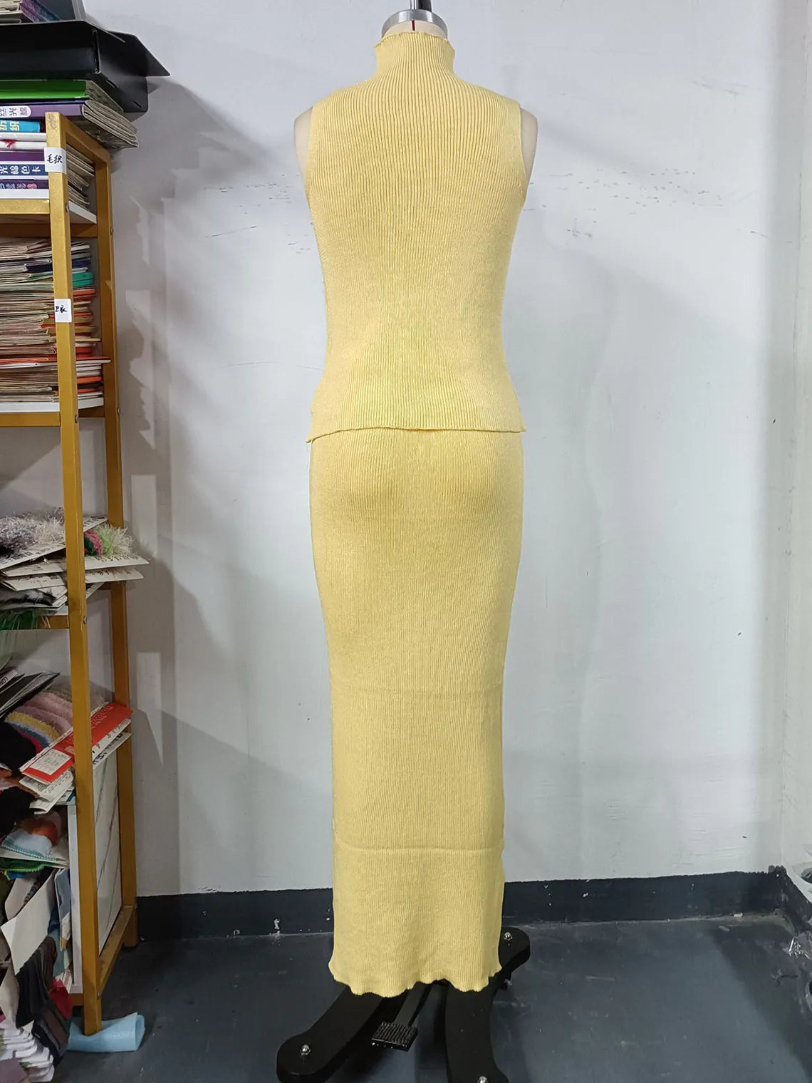 Yellow dress on a mannequin against a white wall with a bookshelf in the background. #Color_Yellow