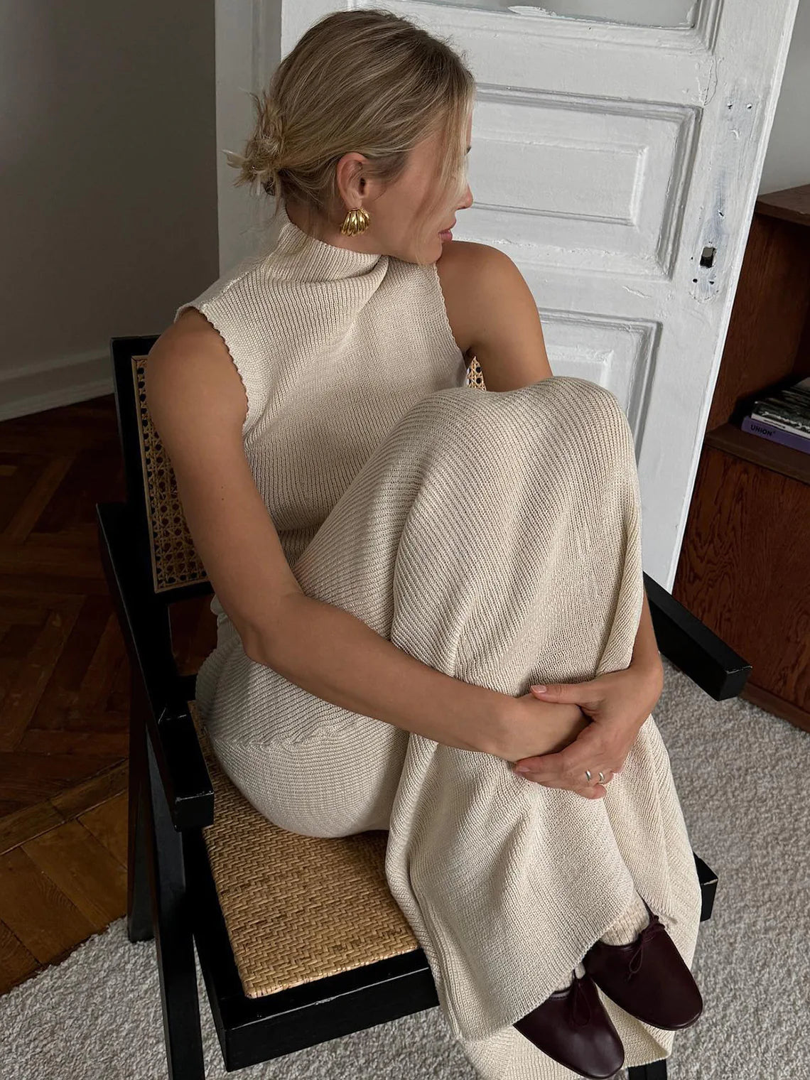 Woman sitting on a chair holding a beige blanket in a room with a white door. #Color_Beige